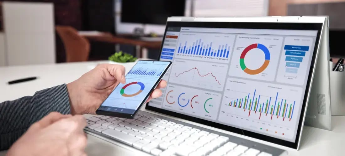 A manufacturing manager reviews real-time production analytics on a laptop and mobile device, using cloud-based Manufacturing Execution System (MES) software to track performance, identify bottlenecks, and optimize operations in a Manufacturing 4.0 environment.